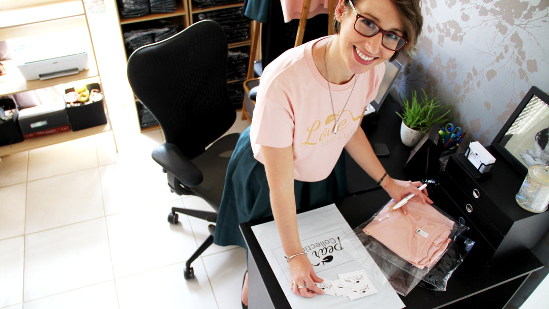 Woman in a pink shirt working at a desk with a laptop and various items.