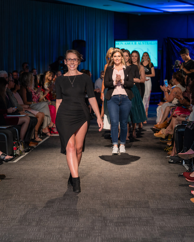Model walking on a fashion show runway with an audience on either side.