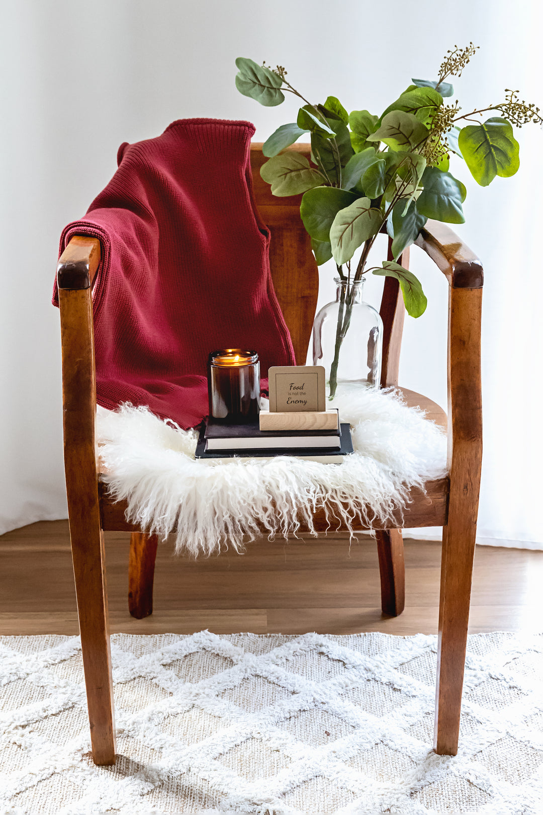 Wooden chair with a red blanket, candle, and plant on a white rug.