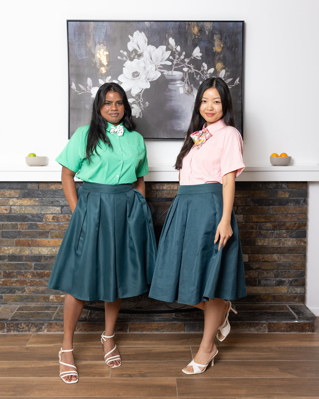 Two women in matching outfits standing in a room with a decorative painting on the wall.