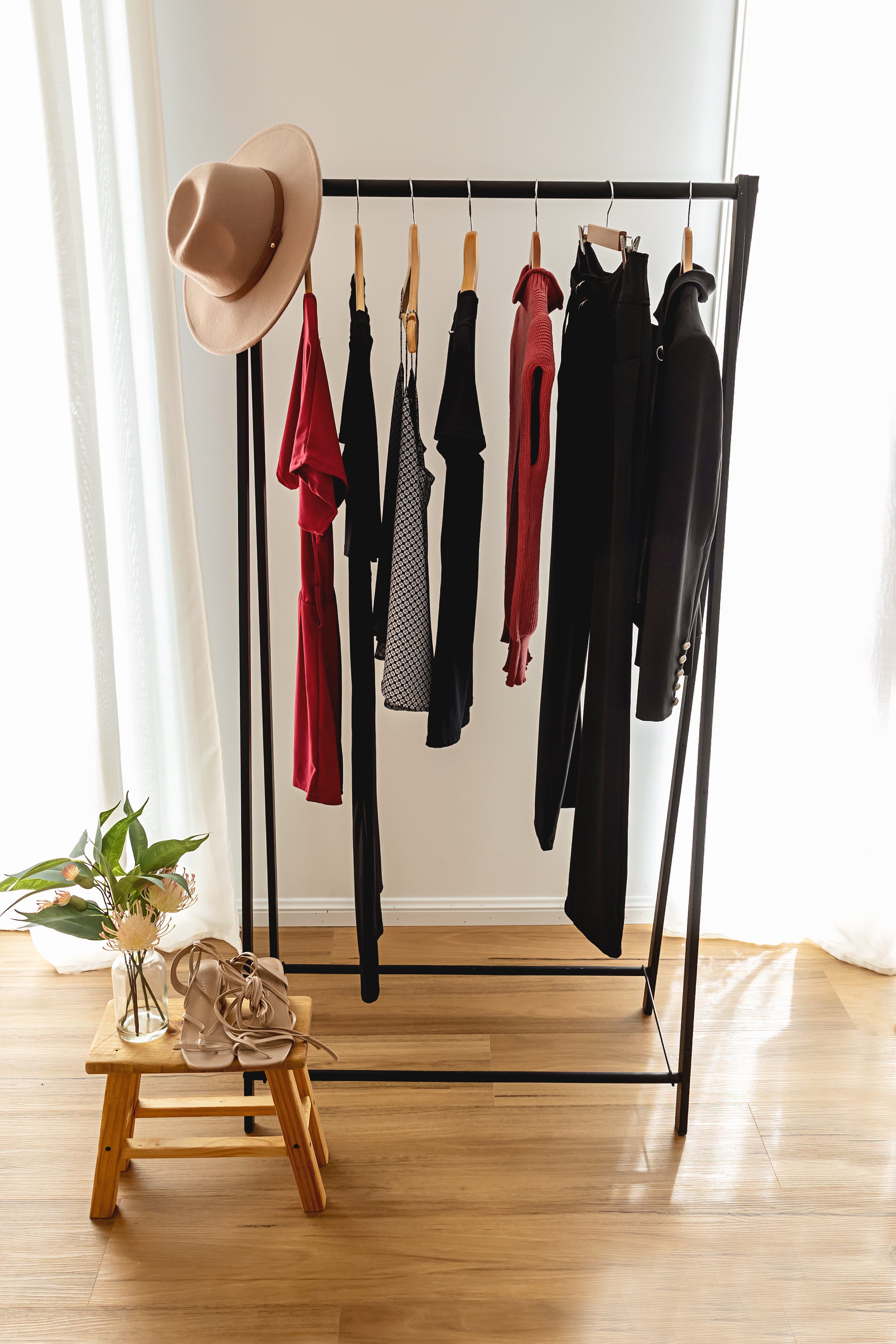 Clothing rack with clothes and a hat on a wooden floor.