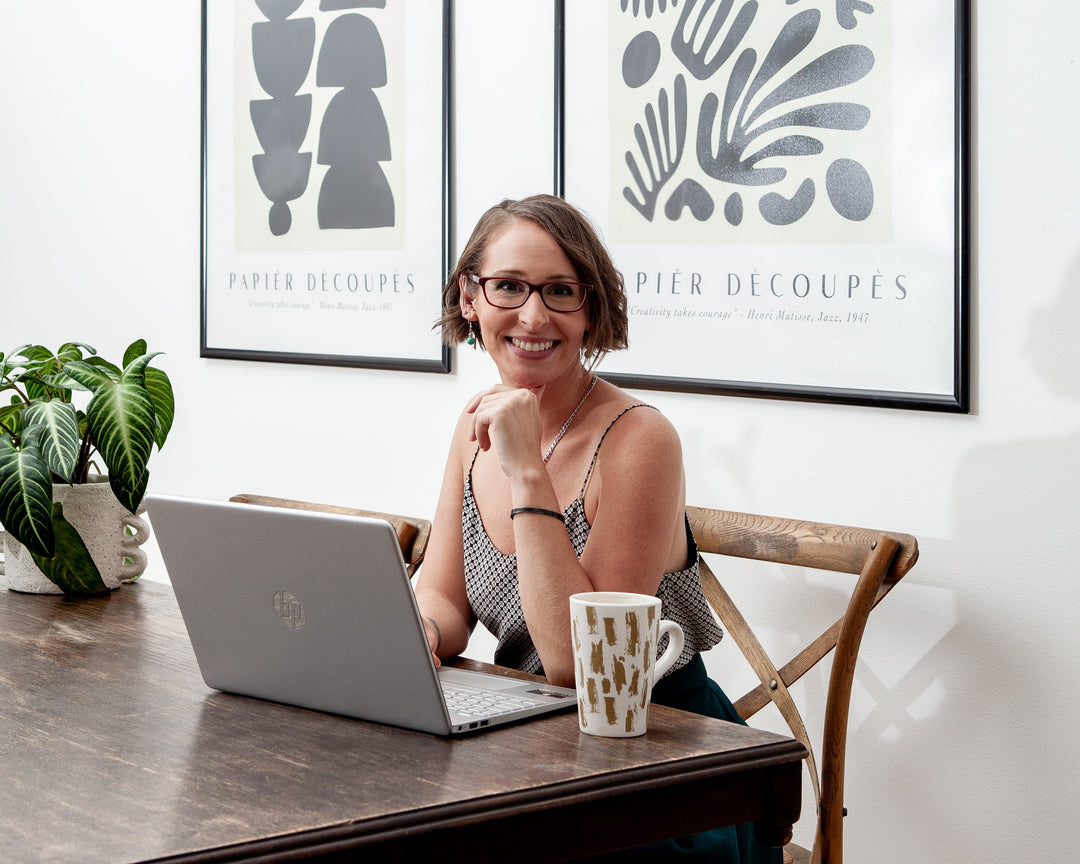 Woman sitting at a desk with a laptop, surrounded by framed art on the wall.