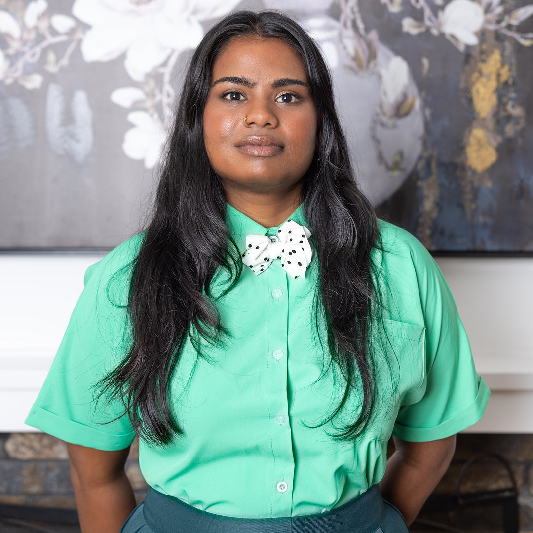 Woman wearing a green shirt with a decorative collar in front of a floral painting.